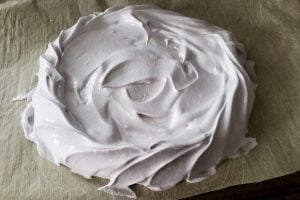 A mound of meringue on a baking sheet lined with parchment paper. It has been swirled into a circle.