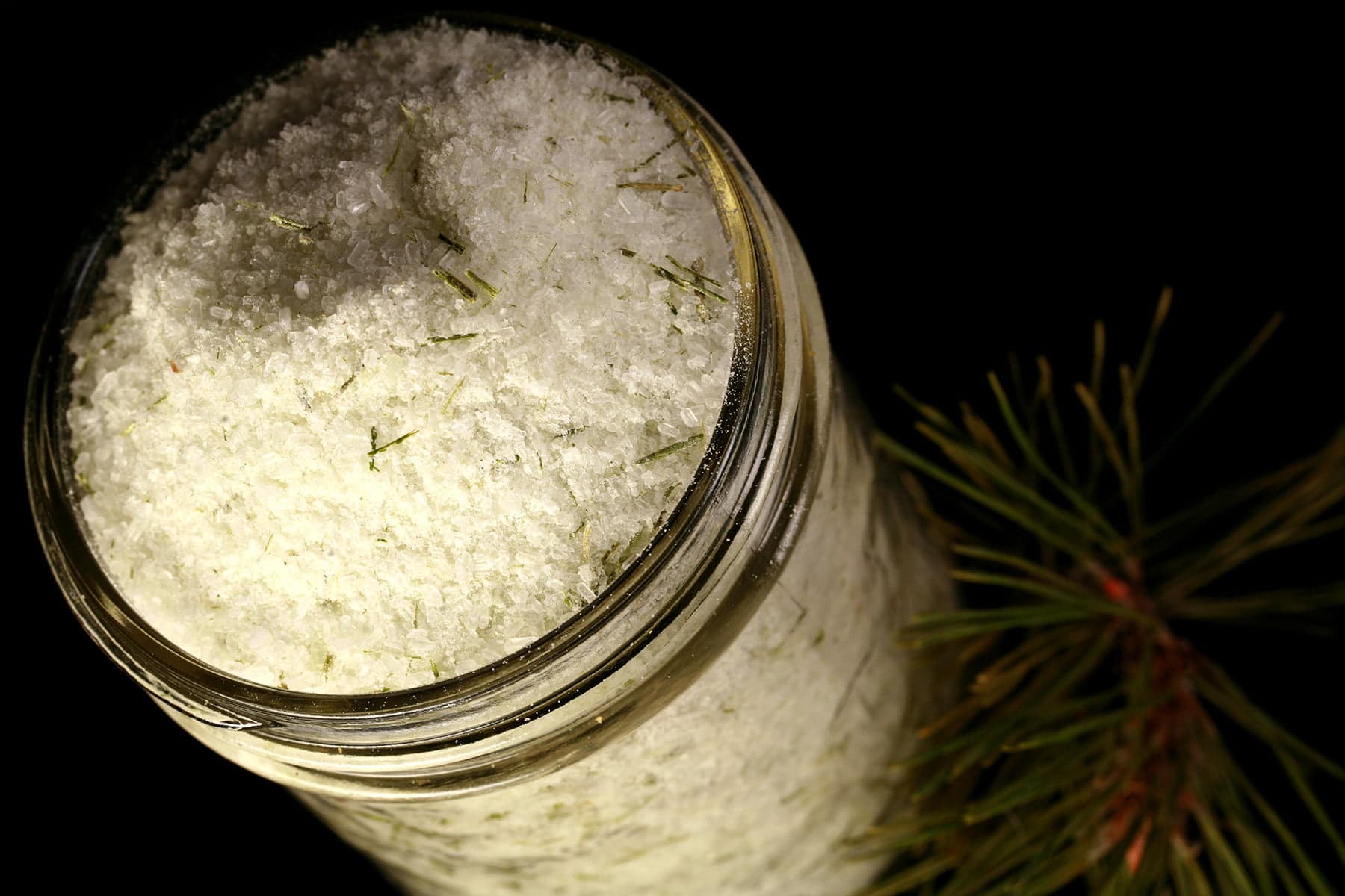 A mason jar filled with a pale green salt that has green flecks of pine needles throughout.