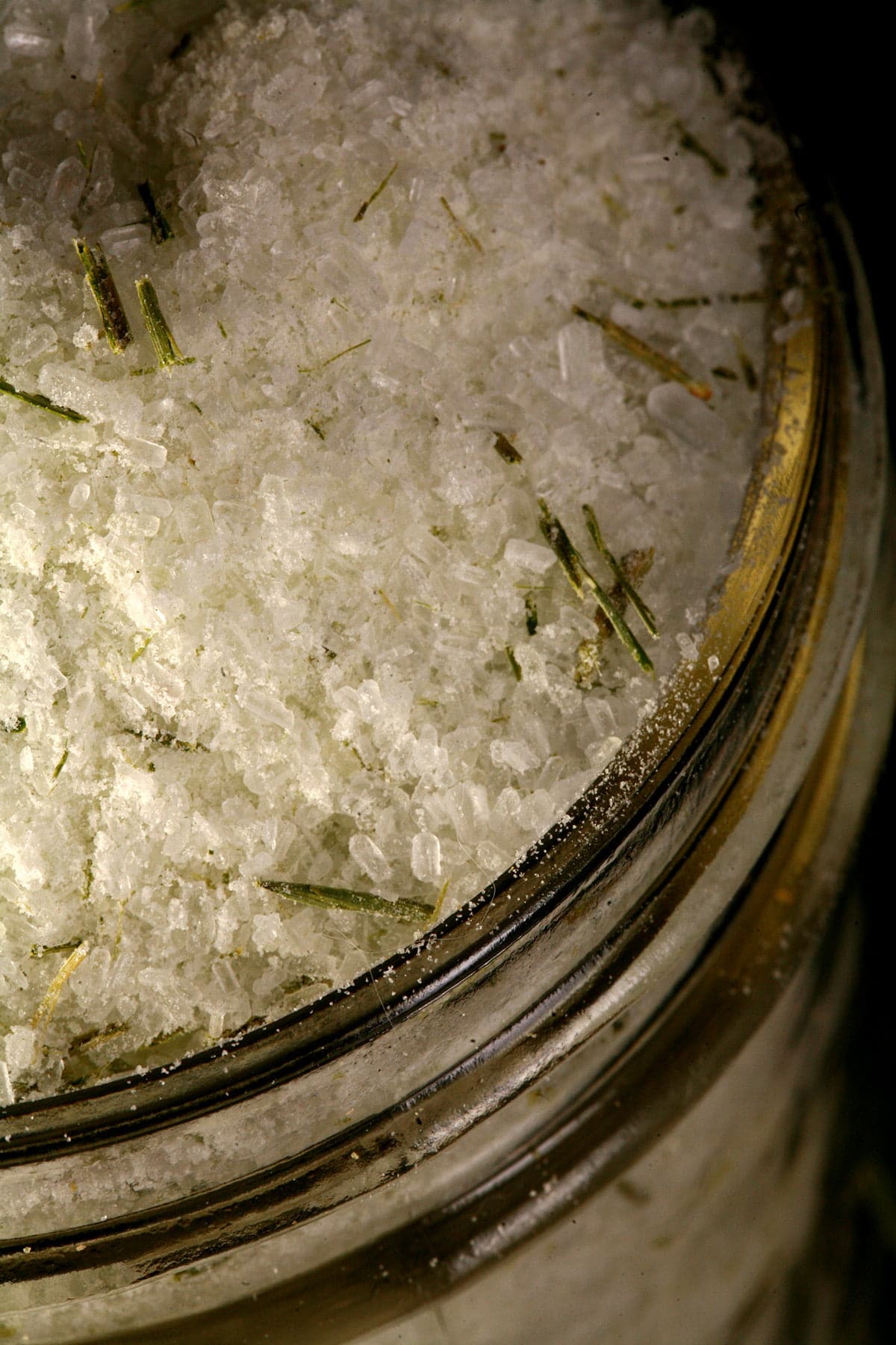 A mason jar filled with a pale green salt that has green flecks of pine needles throughout.