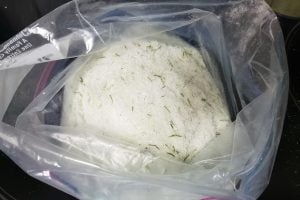 A large plastic baggie filled with a pale green salt that has green flecks of pine needles throughout. It is standing open.