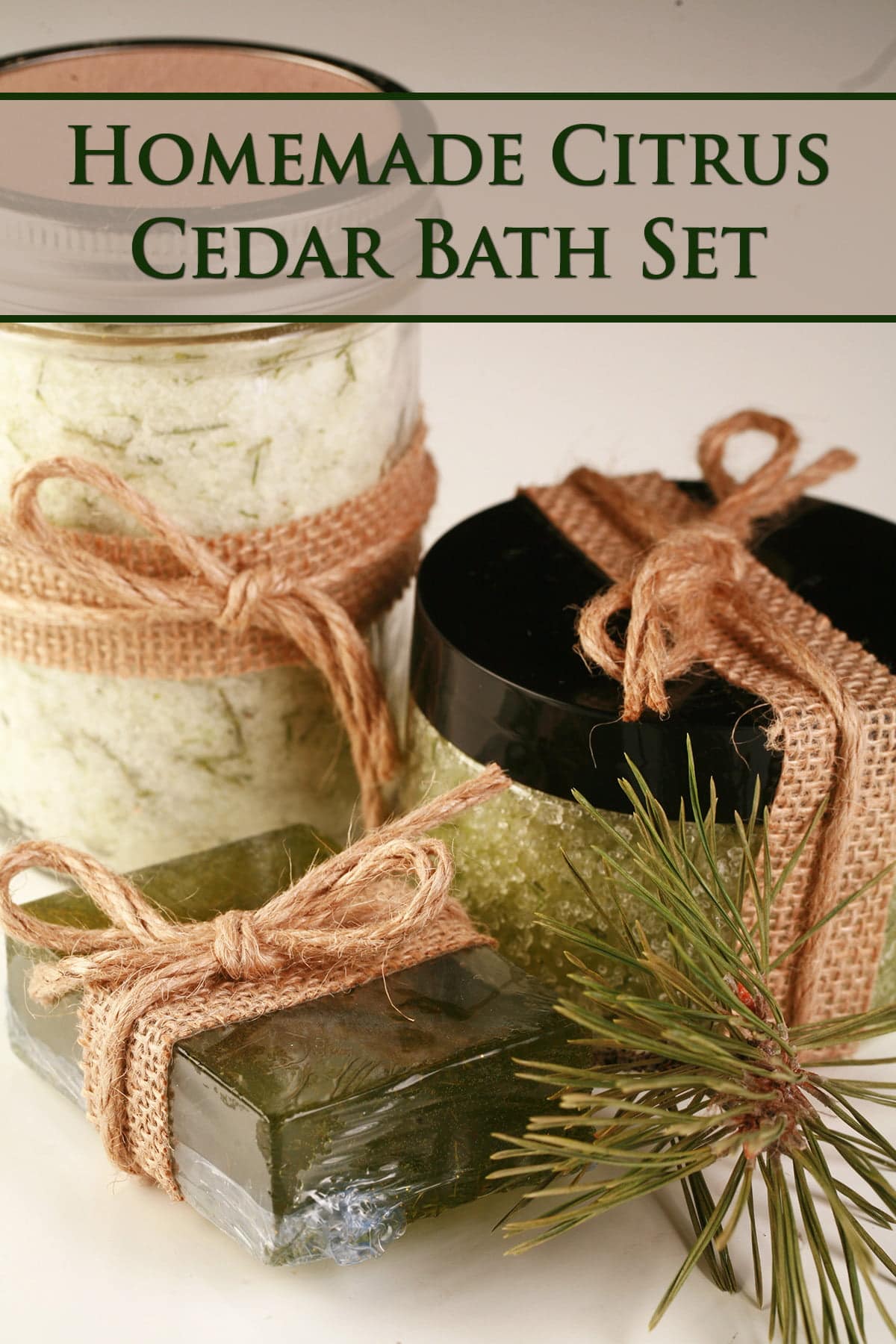 A trio of cedar bath products - a mason jar with bath salts, a smaller jar with green salt scrub, and a green bar of soap. All have flecks of preen pine needles in them. All 3 items are wrapped with burlap ribbon and tied with twine.