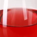 Close up photo of a glass of brilliantly red cranberry wine, in front of a white background.