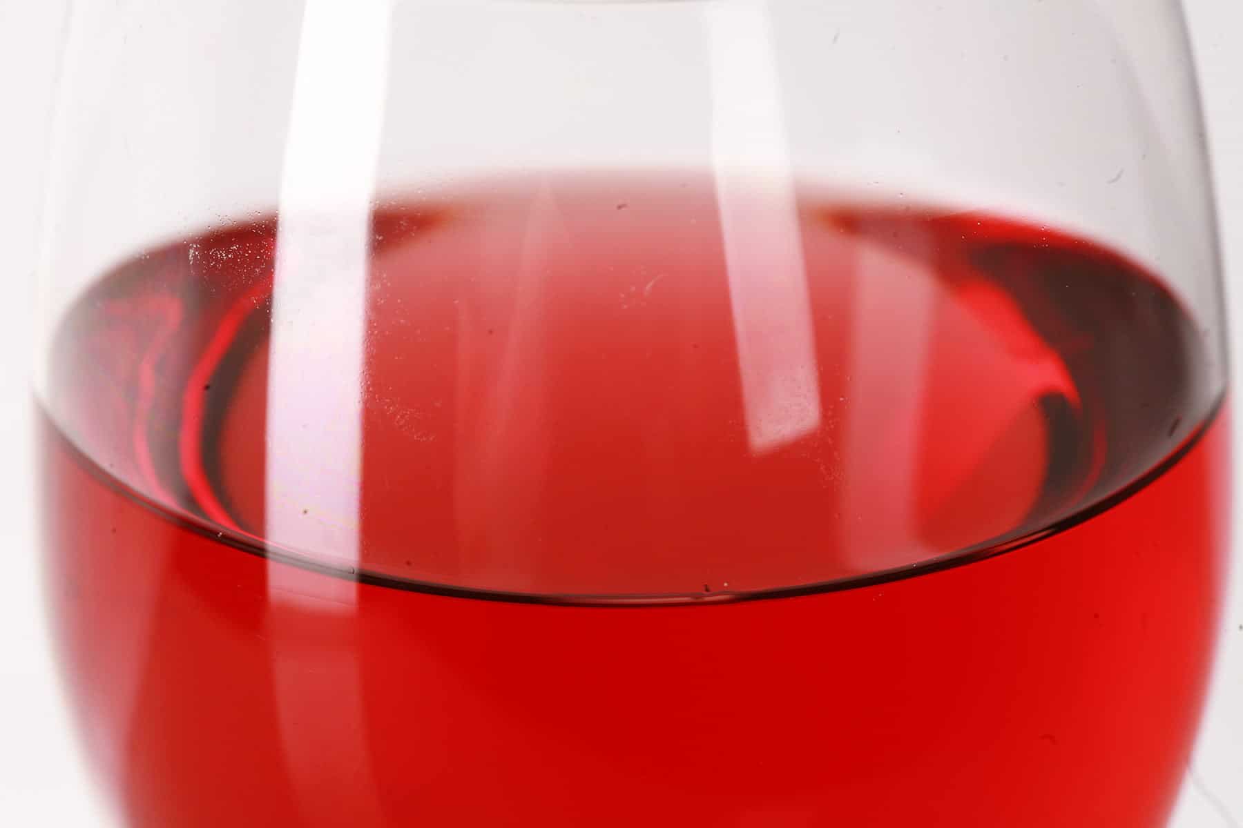 Close up photo of a glass of brilliantly red cranberry wine, in front of a white background.