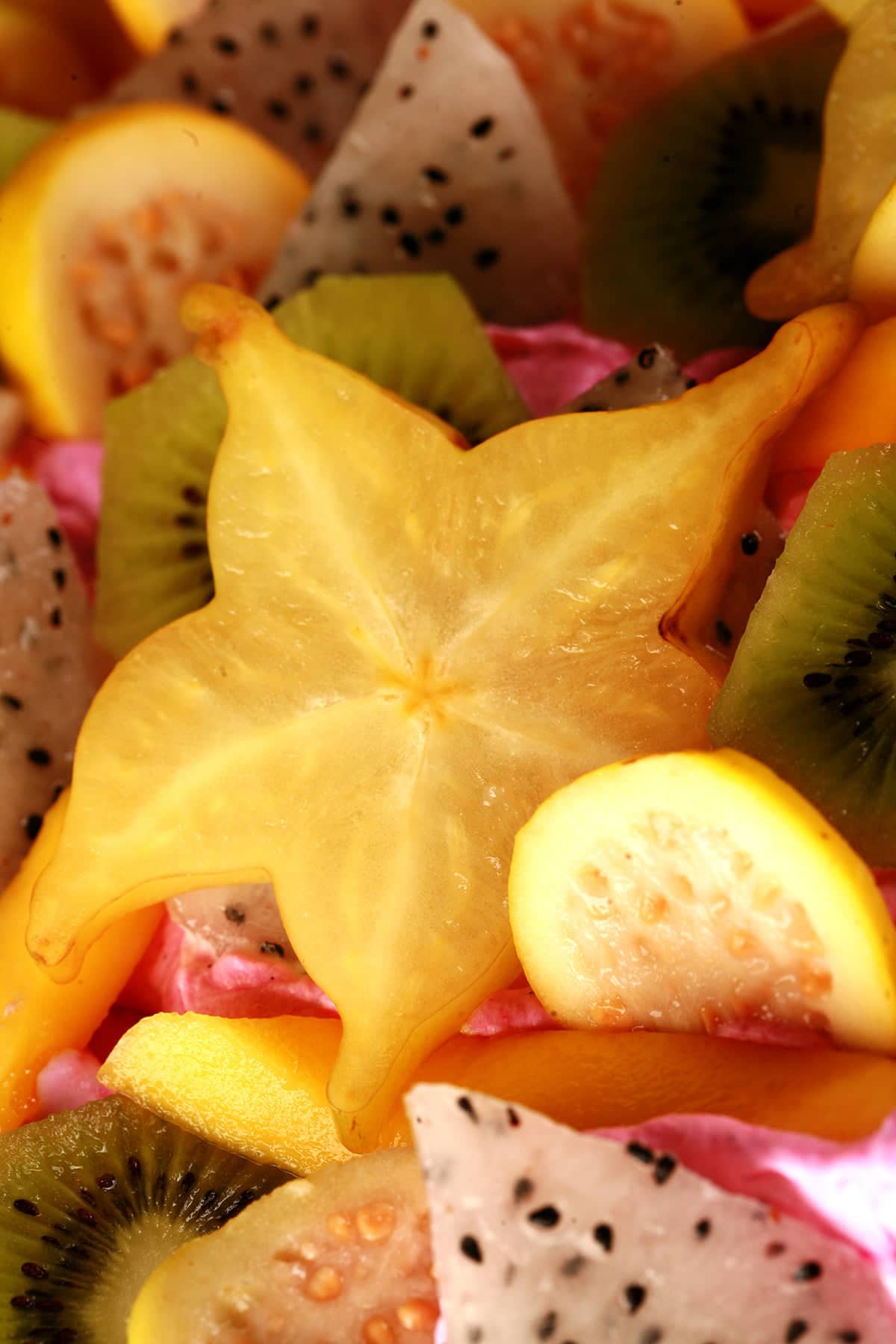 Close up view of slices of star fruit, kiwi, and guava, nestled in bright pink whipped cream.