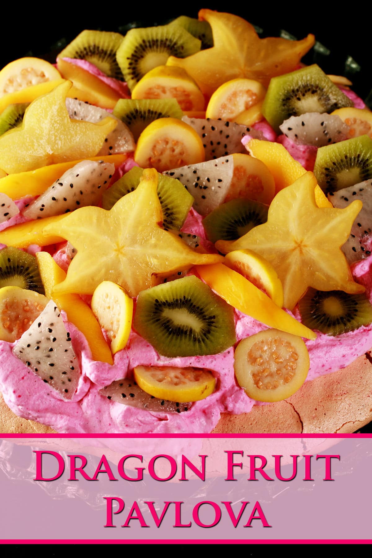 Close up view of a colourful pavlova. It has a light pink meringue base, bright pink whipped cream, and is topped with dragon fruit, star fruit, guava, and mango.