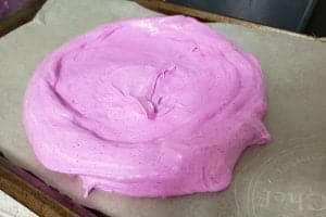 A round of bright pink raw meringue, on a cookie sheet lined with parchment paper.