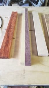 Several small strips of different colored wood on a table. Two strips are joined together.