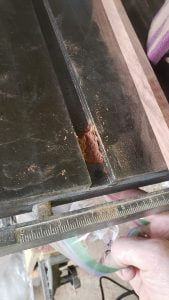 A metal table saw work surface is seen, with a slot. Some wood dust is gathered into the slot.