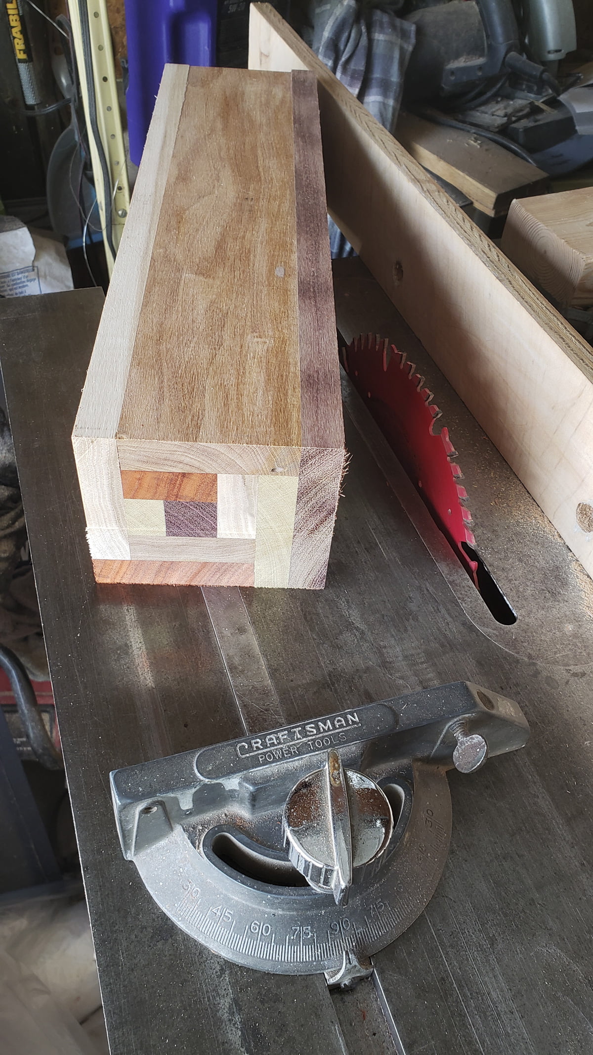 A rectangular block, made from several smaller pieces of different colored wood, is on top of a table saw.