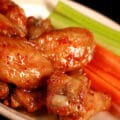 A small plate of maple dijon wings, with carrot and celery sticks on the side.