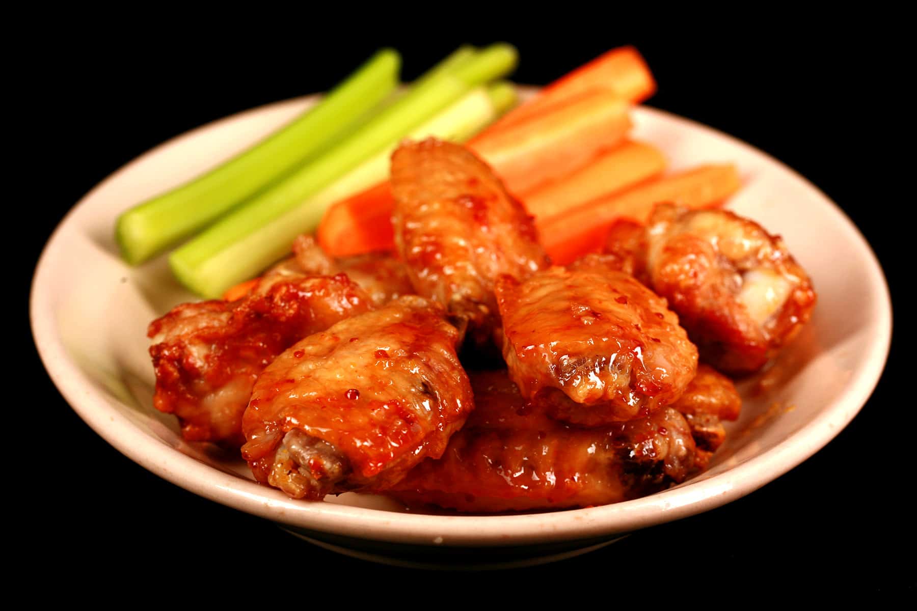 A small plate of maple dijon wings, with carrot and celery sticks on the side.