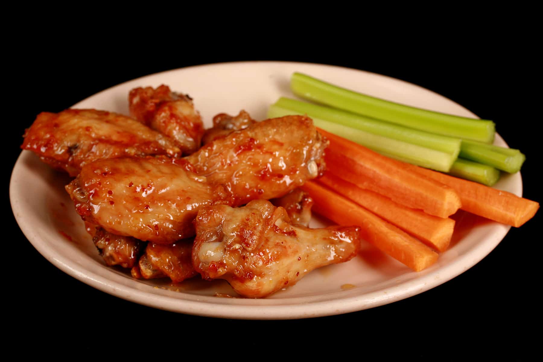 A small plate of maple dijon glazed wings, with carrot and celery sticks on the side.