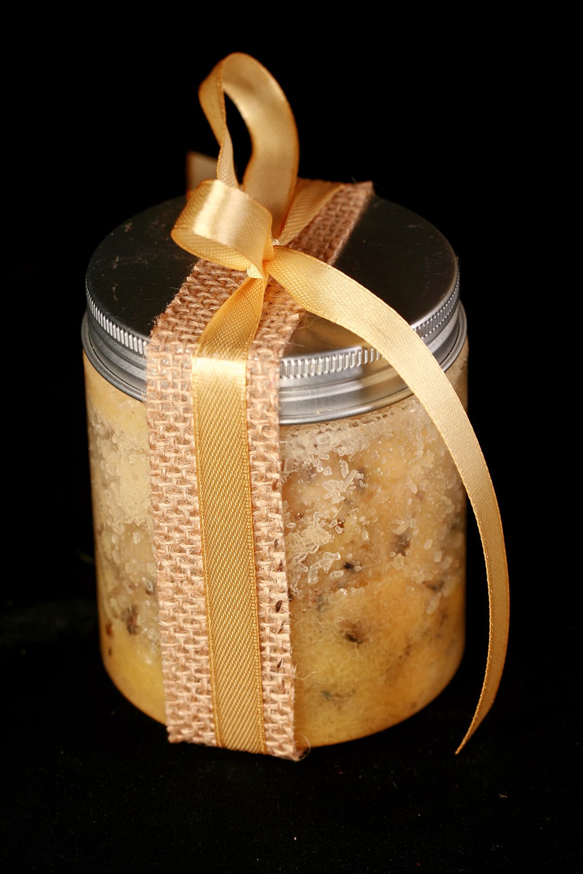 A small jar of mustard bath salt scrub. It is tied with a yellow bow.