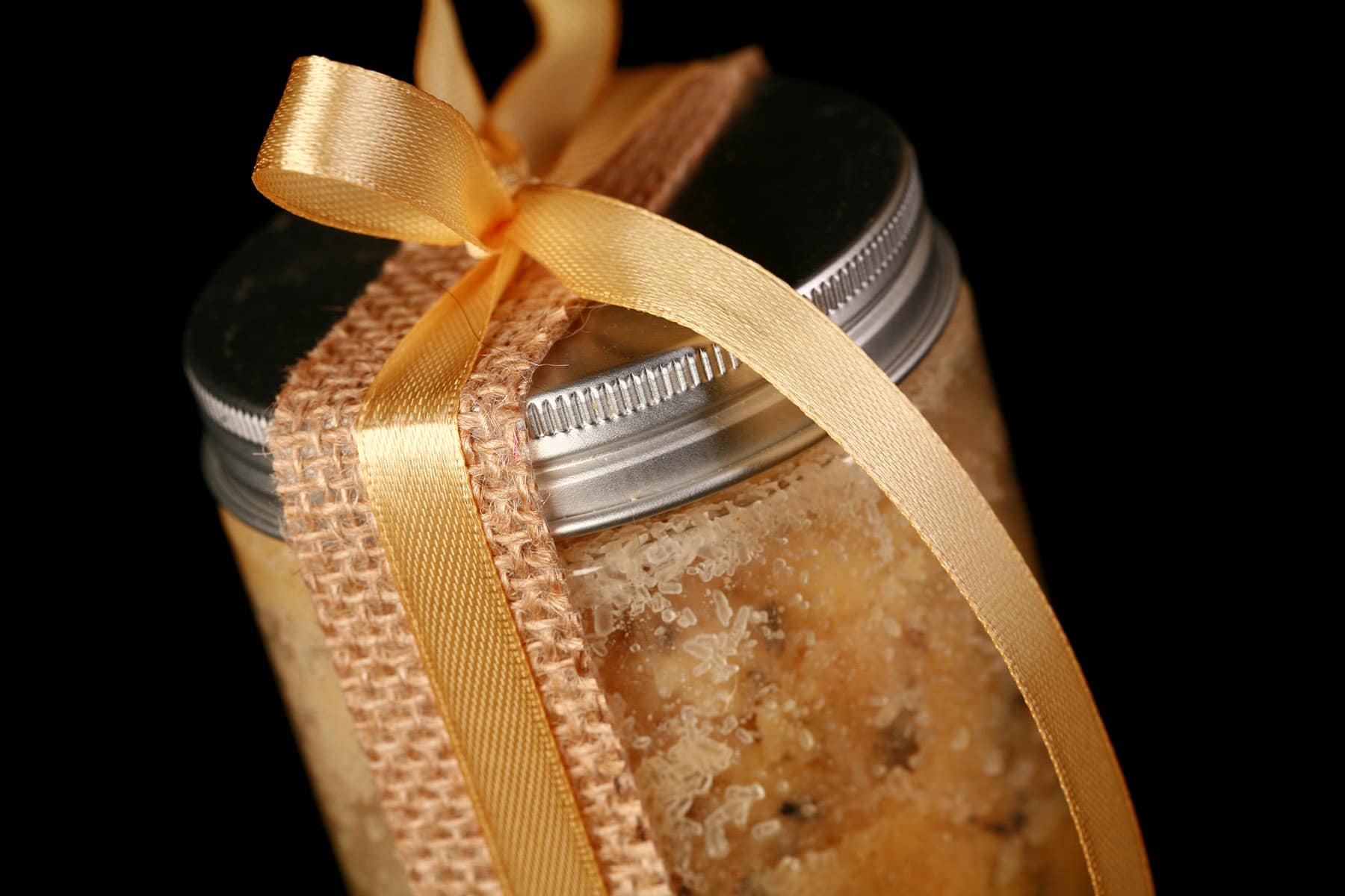 A small jar of mustard bath salt scrub. It is tied with a yellow bow.