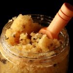 Close up view of a small jar filled with yellow salts and a small wooden scoop