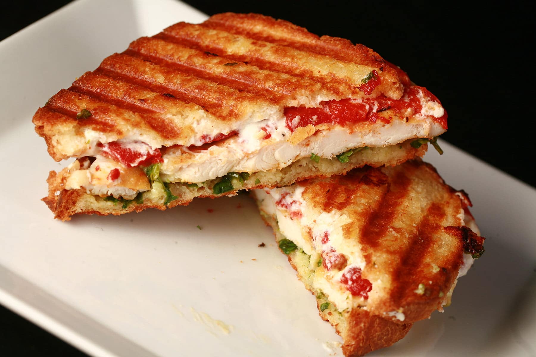Close up view of a chicken panini sandwich. It's sliced in half, and roasted red pepper, chicken breast, goat cheese, and pesto layers are visible.