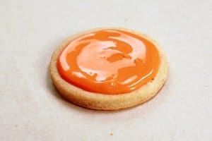 A single round cookie, with orange frosting covering the top.