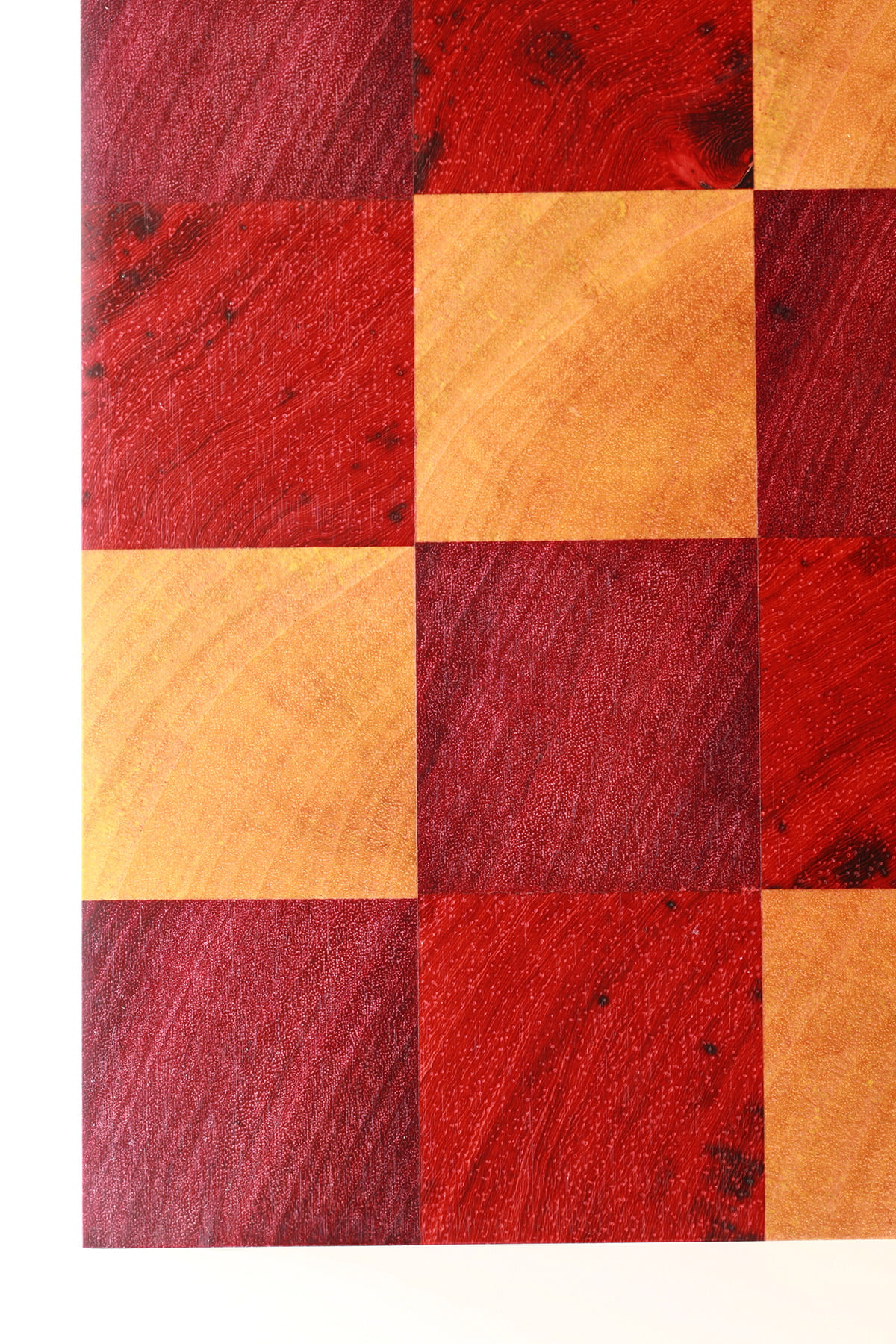 A close up view of a DIY cutting board, made up of colourful squares of wood - red, purple, and yellow.