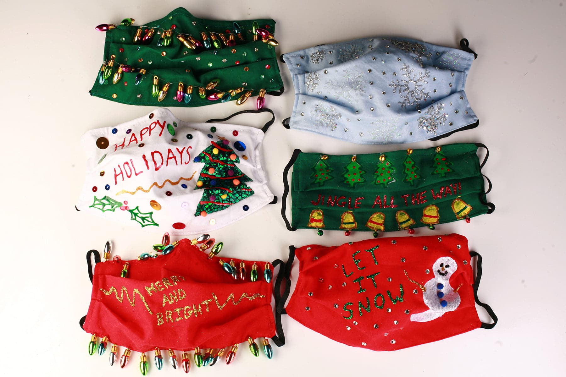 An array of 6 gaudily decorated "Ugly Christmas Sweater" style face masks, on a white background.