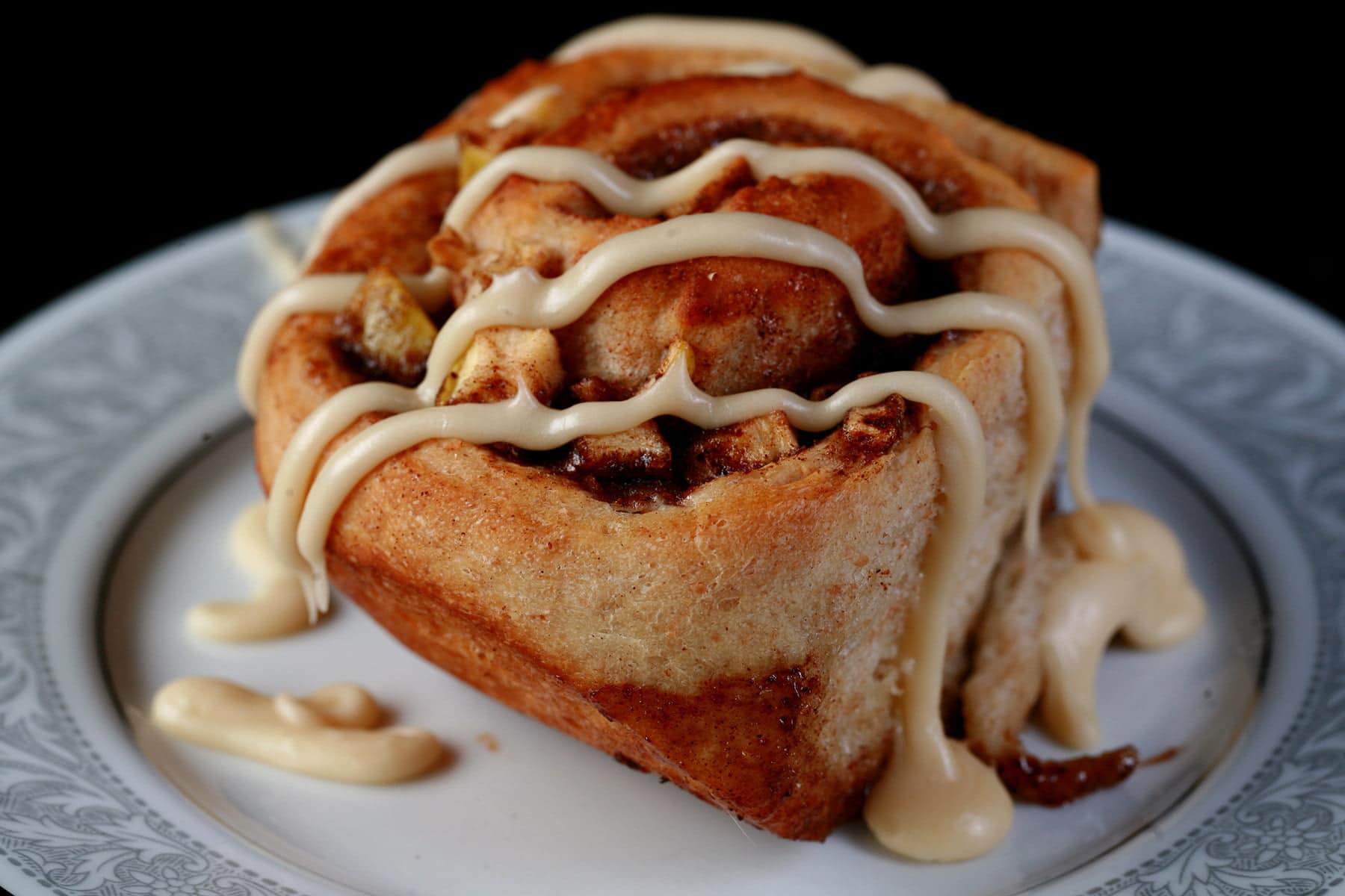 Close up photo of an apple cinnamon bun - a cinnamon bun, with small pieces of apple throughout the cinnamon swirl - drizzled with maple glaze.