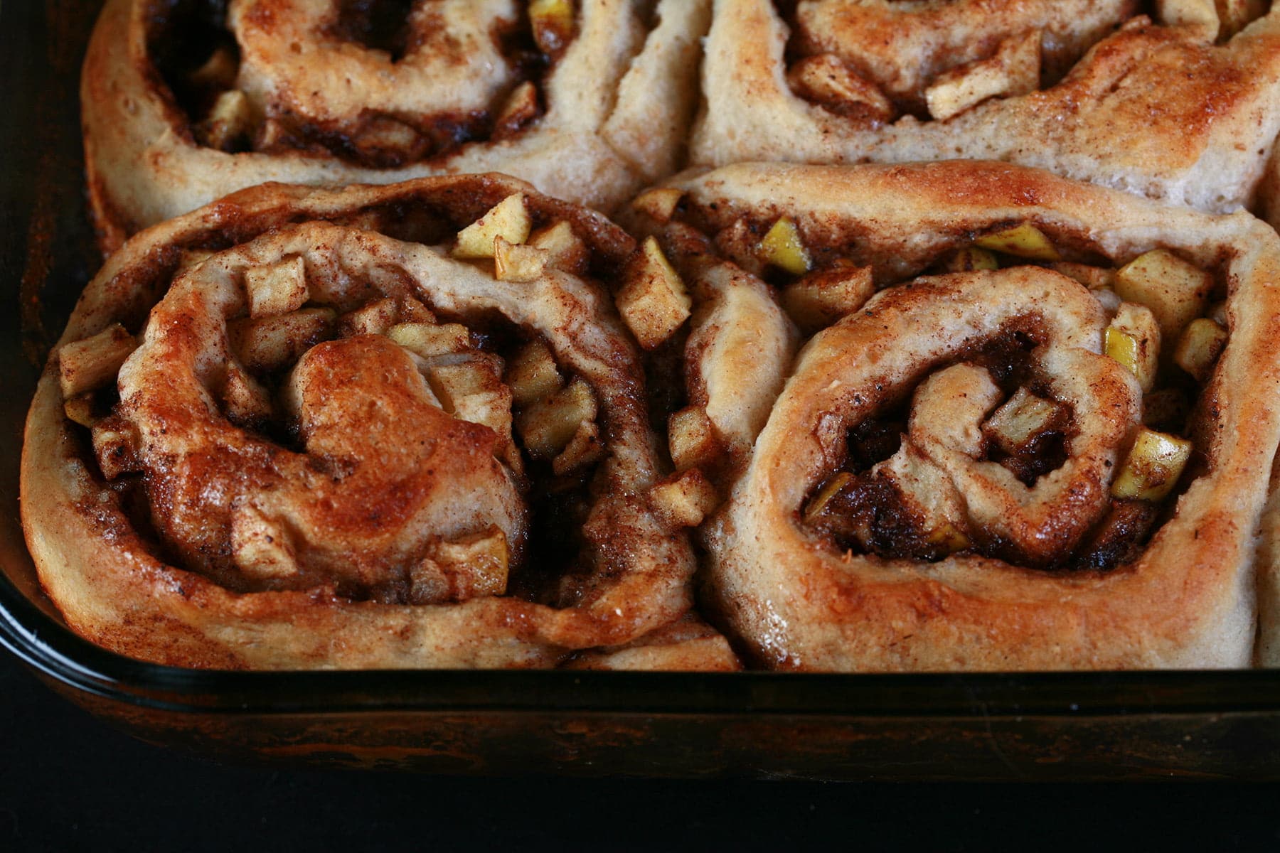 Close up photo of a pan of apple cinnamon buns - cinnamon buns, but with small pieces of apple throughout the cinnamon swirl.