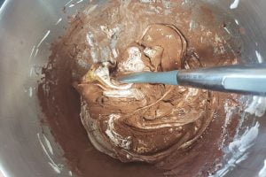 A semi fluid mixture of white meringue and cocoa powder in a bowl.