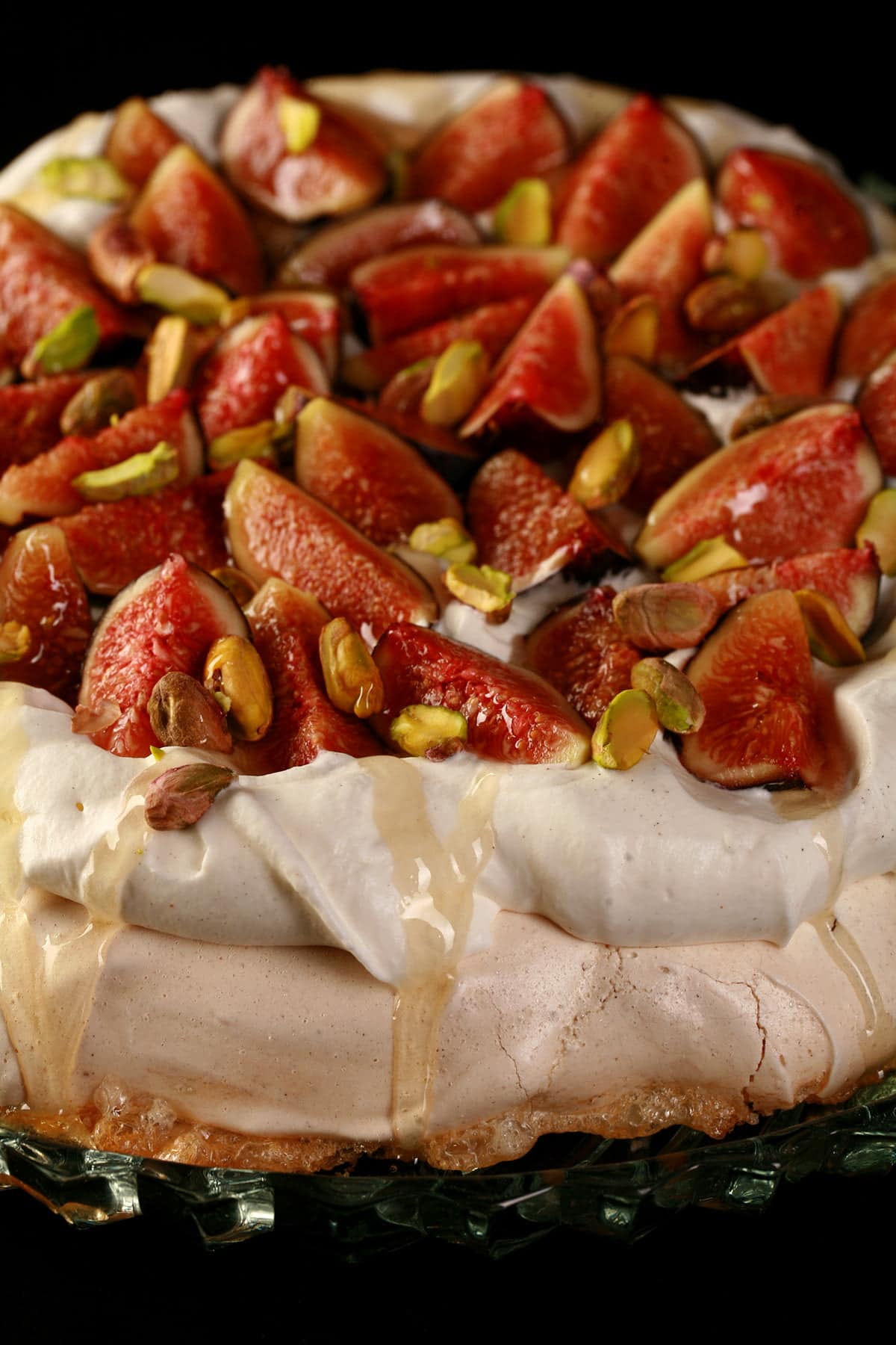 An ivory coloured meringue round, piled with whipped cream, sliced figs, and pistachios. A drizzle of honey finishes it off.