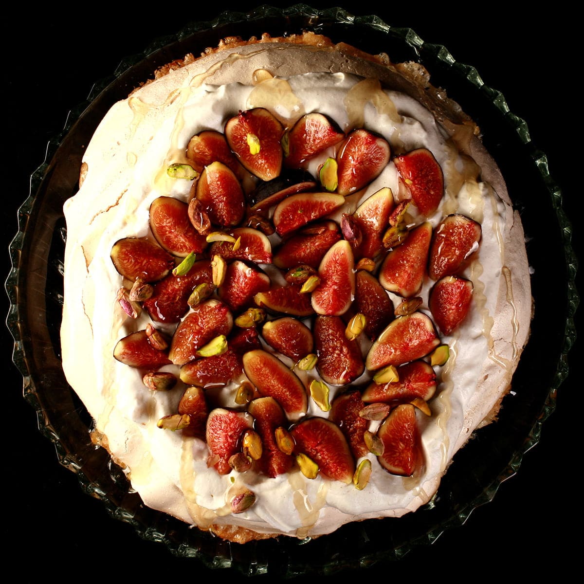 An ivory coloured meringue round, piled with whipped cream, sliced figs, and pistachios. A drizzle of honey finishes it off.