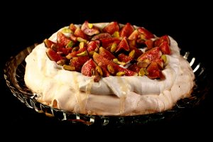 An ivory coloured meringue round, piled with whipped cream, sliced figs, and pistachios. A drizzle of honey finishes it off.