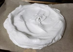 A circle of swirled, shiny white meringue on a parchment lined baking sheet.