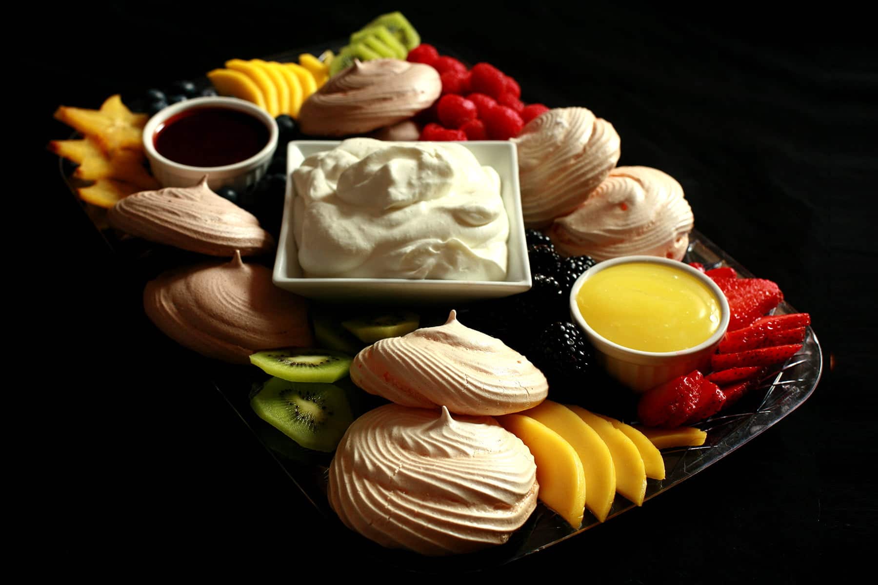 A pavlova dessert board, with mini pavlovas, fruit, curds, and whipped cream.