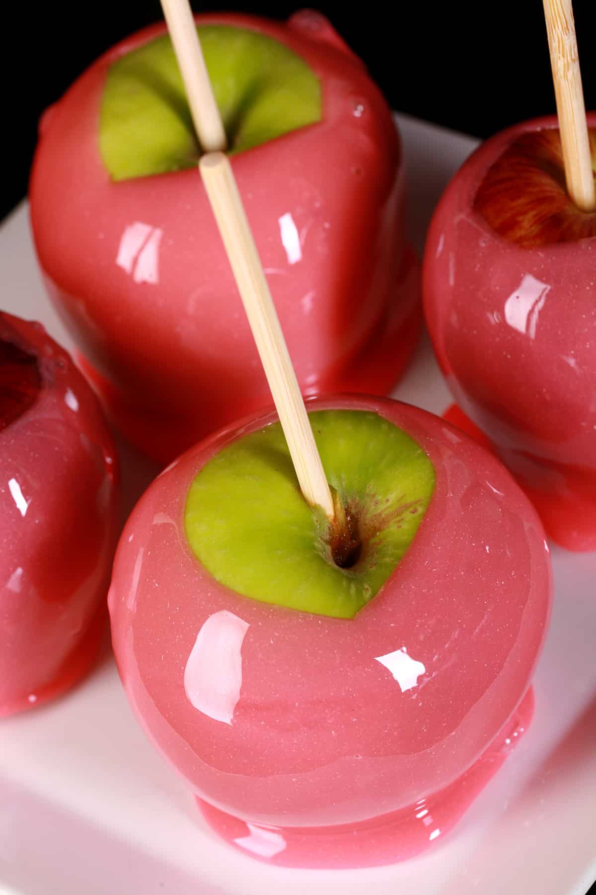 Several pink-coated candy apples on a plate. Half are red apples, the other half are green.