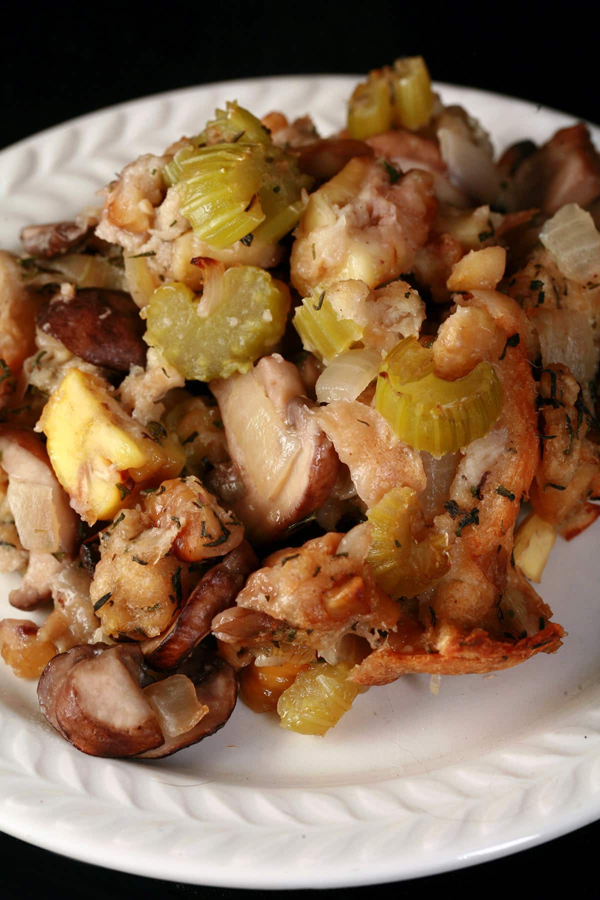 A close up view of a plate of stuffing with chestnuts, mushrooms, and celery visible.
