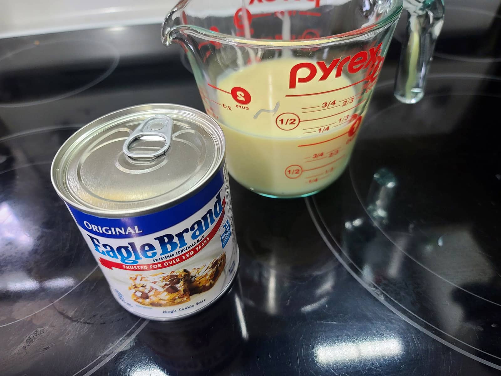 A can of sweetened condensed milk next to a measuring cup of sweetened condensed milk.