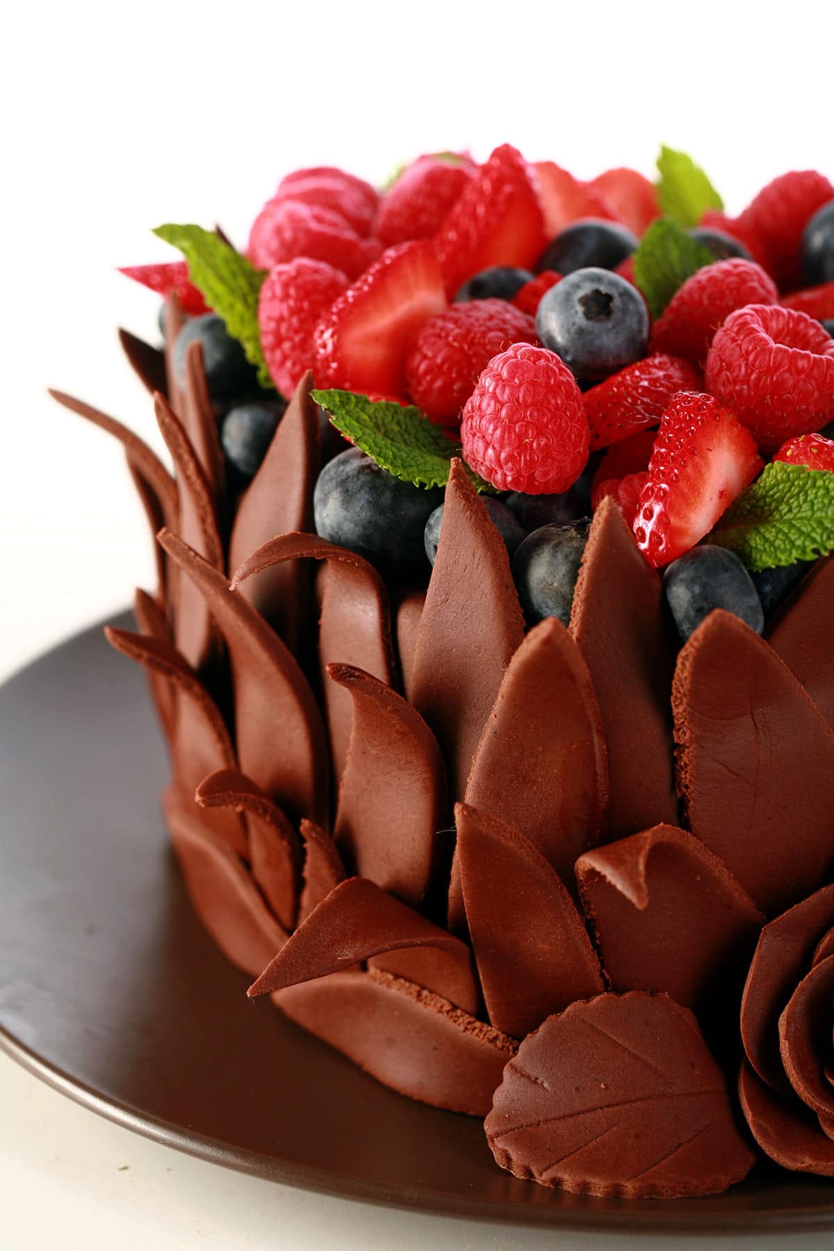 A heart shaped cake, covered in chocolate fondant leaves. The top of the cake is covered with a pile of fresh berries and mint leaves.