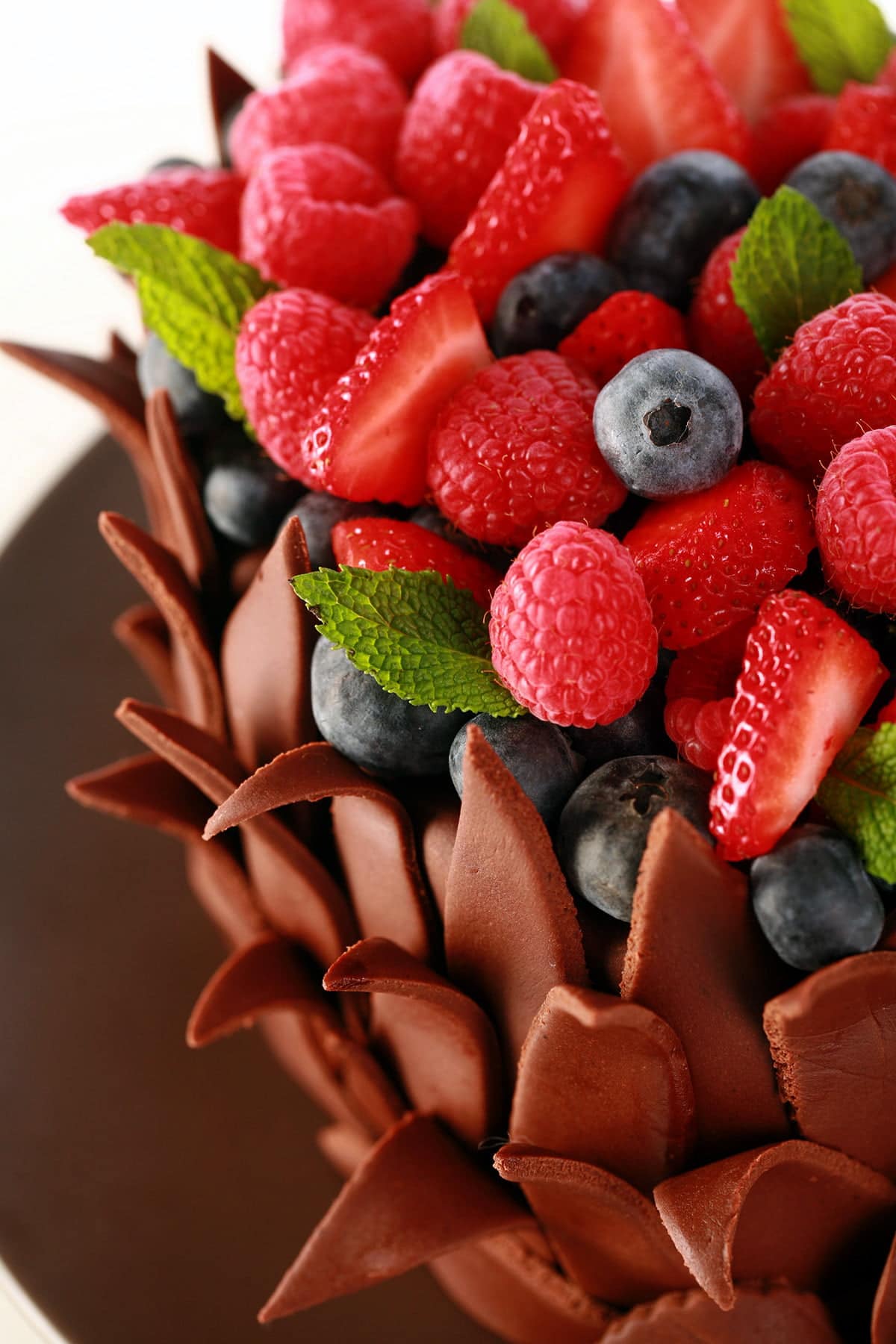 A heart shaped cake, covered in chocolate fondant leaves. The top of the cake is covered with a pile of fresh berries and mint leaves.