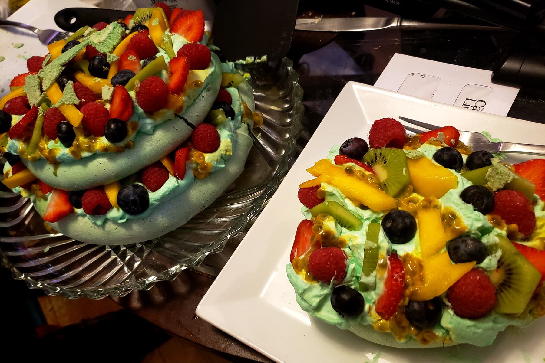 One layer of the pavlova is on a plate, next to a partially dismantled main pavlova.