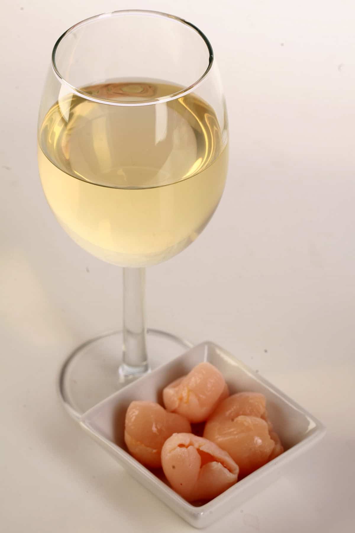 A glass of white wine - made from this lychee wine recipe - is pictured next to a small bowl of lychee fruit.