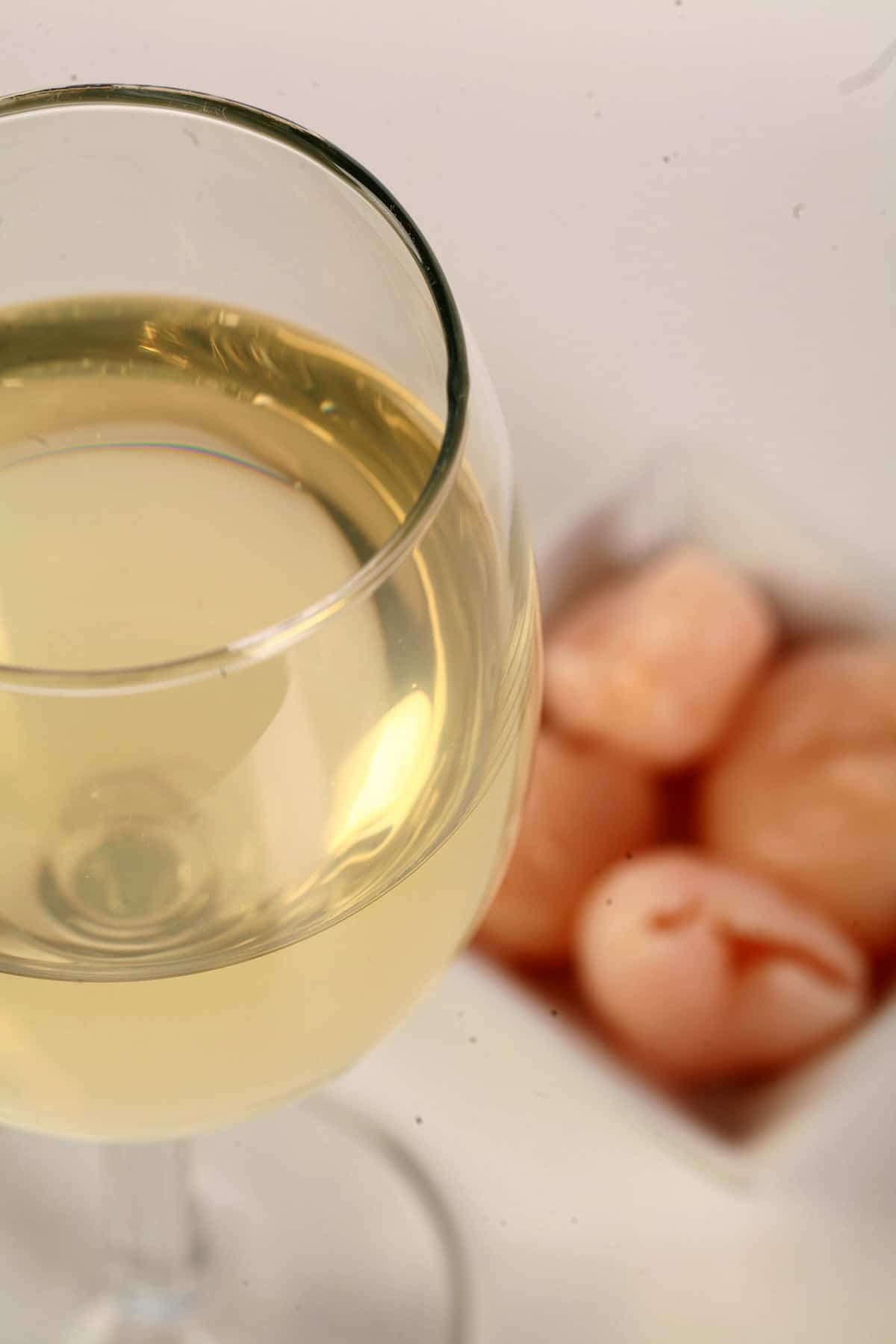A glass of white wine  - made from this lychee wine recipe - is pictured next to a small bowl of lychee fruit.