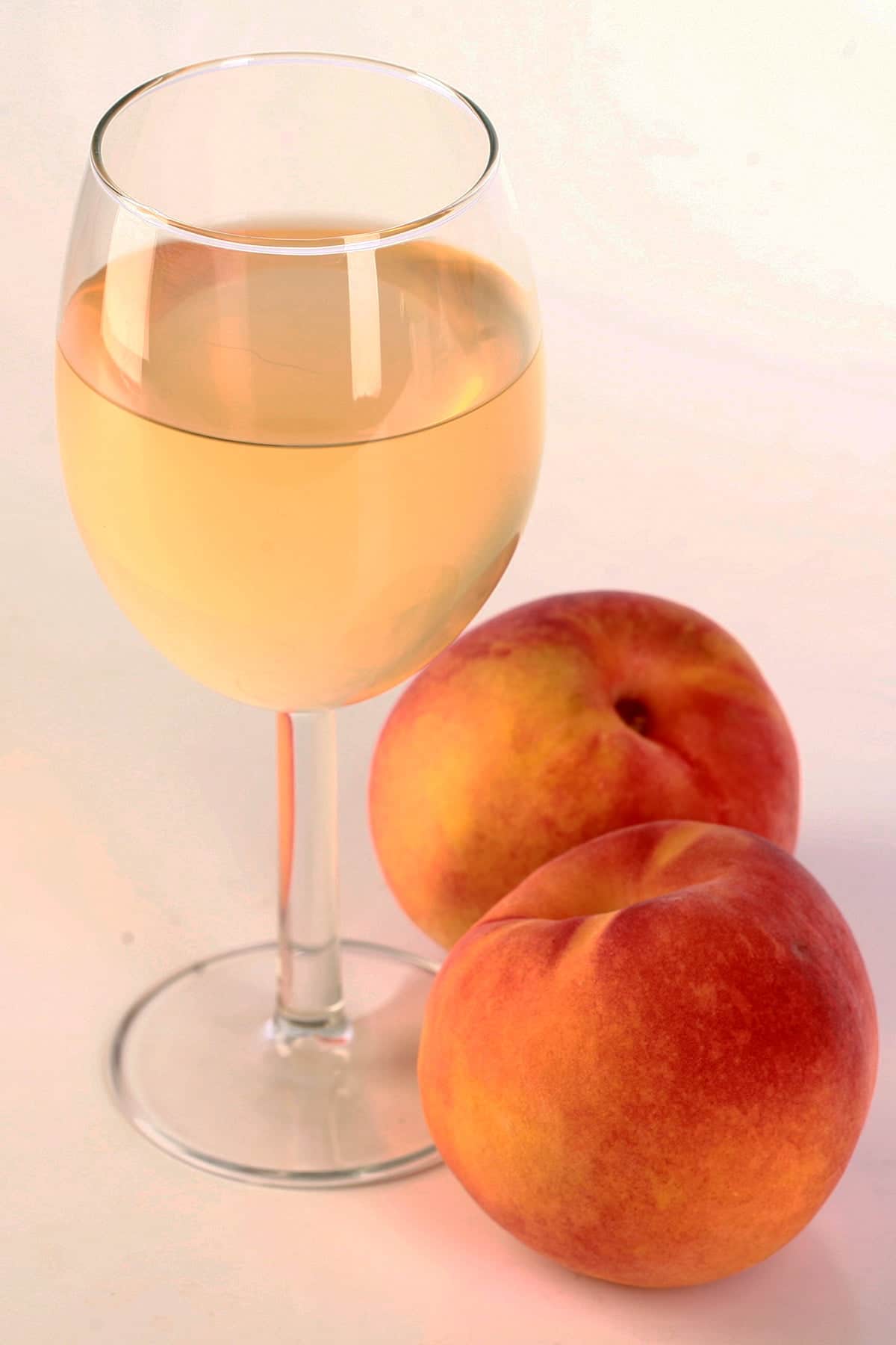 A glass of pale peach coloured wine, with 2 fresh peaches at the base of the glass.