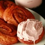 Deep fried cinnamon rolls are arranged on a white platter, one is spread with a pink frosting - A Persian roll!