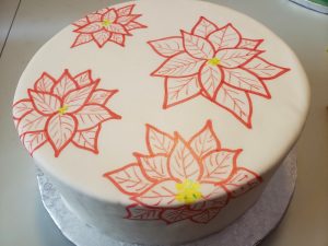 A large round cake covered in smooth white fondant hasred poinsettias drawn all over it.