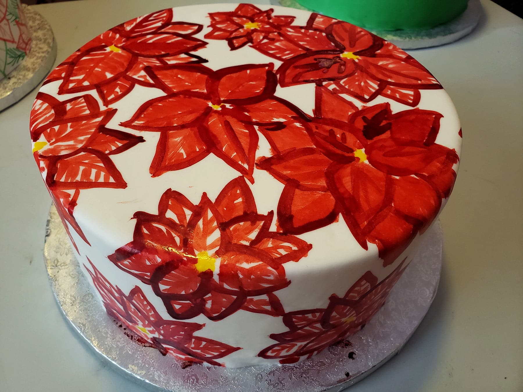 A large round cake is covered in a hand painted poinsetta design, in reds with yellow accents.