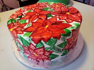 A large round cake is covered in a hand painted poinsetta design, in reds and greens.