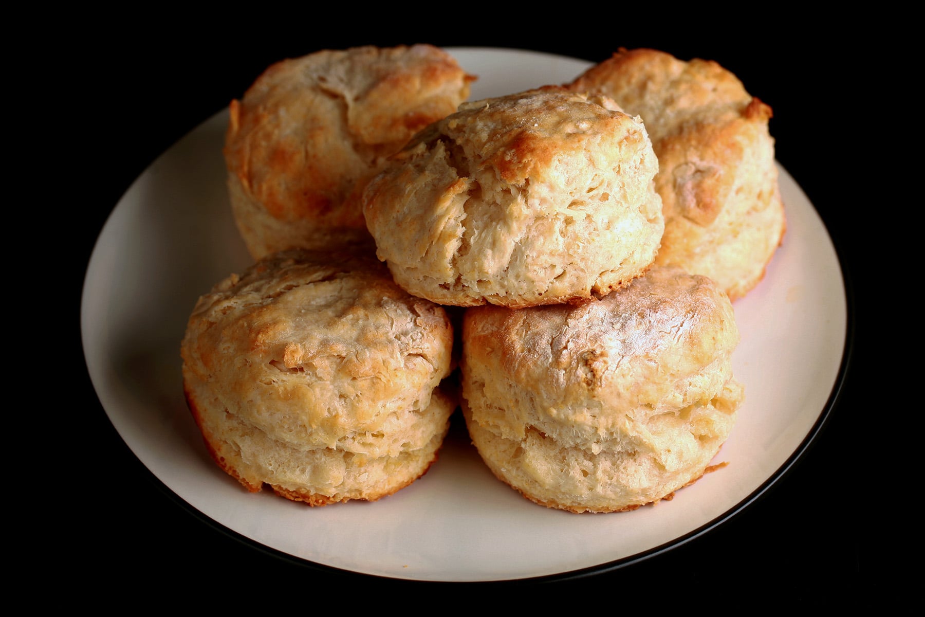 A close up view of several golden baking powder buttermilk biscuits on a plate.