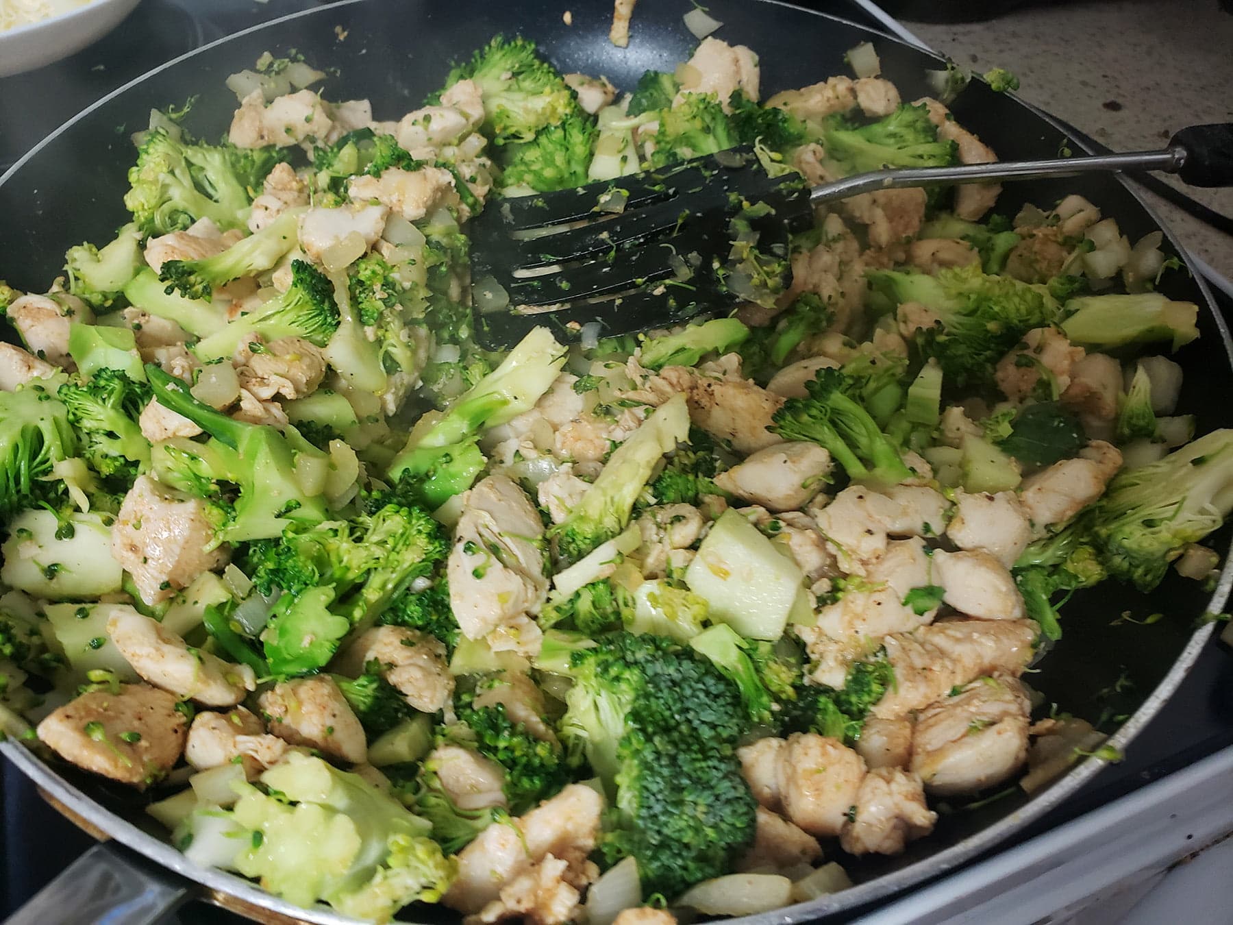 Close up view of a pan of sauteed broccoli, onion, and chicken.