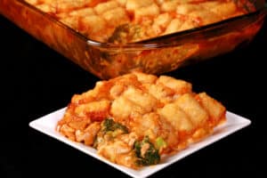A pan and plate of chicken and broccoli casserole with tater tots on top.