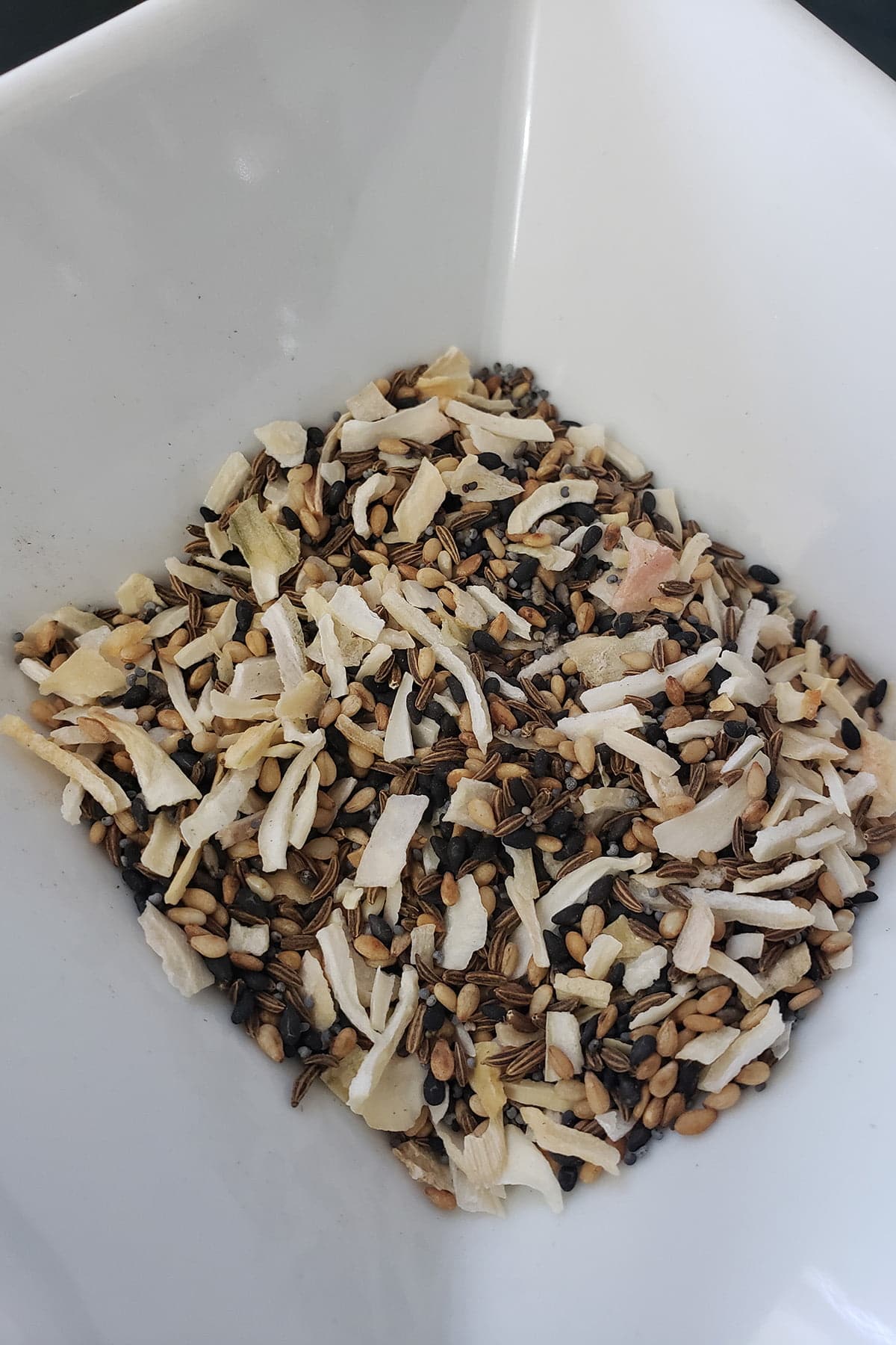 A close up view of a small white bowl filled with "everything" spice mix: Sesame seeds, caraway seeds, onion flakes, garlic flakes, poppy seeds, etc.