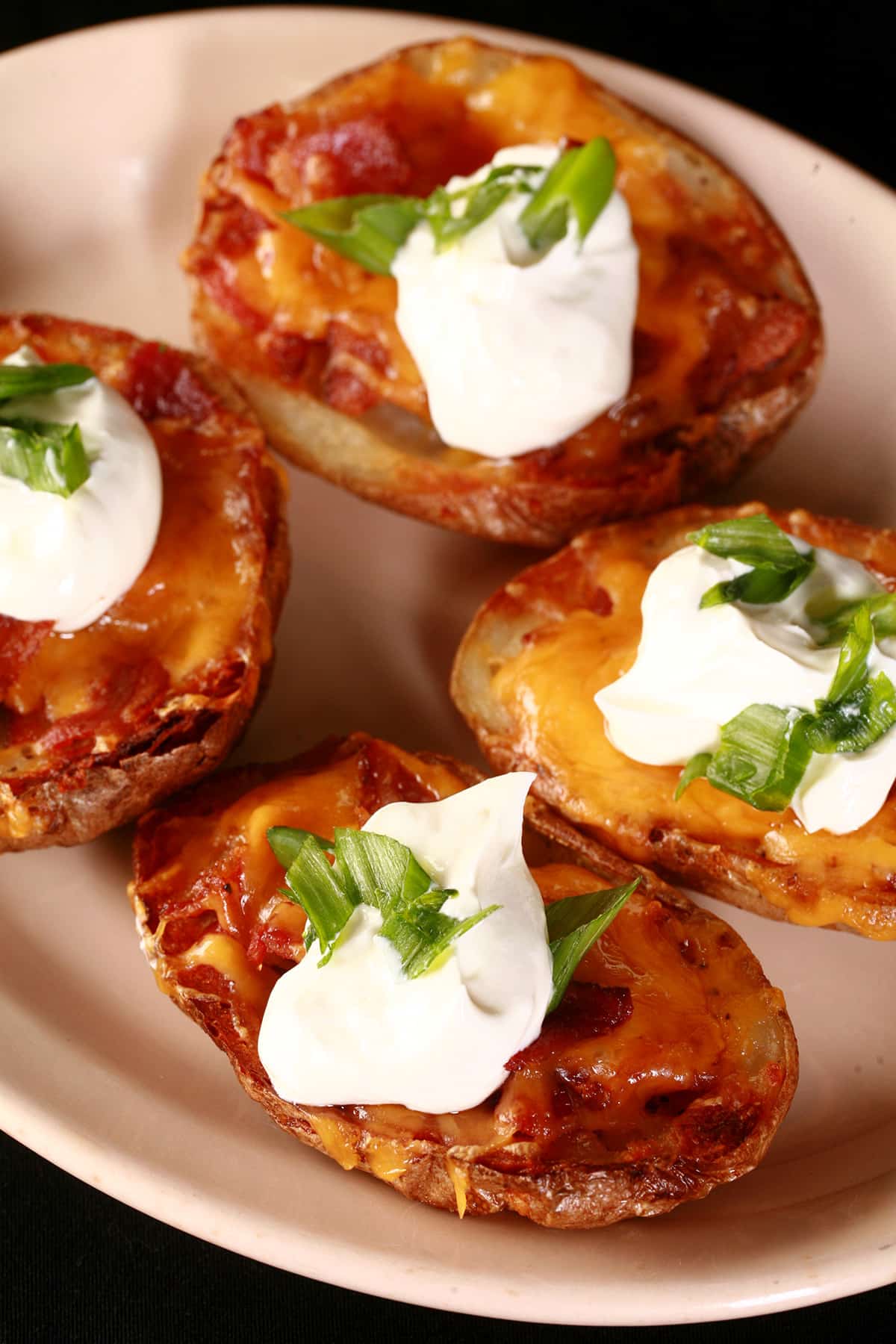 A plate of loaded potato skins topped with bacon, cheddar, sour cream, and sliced green onions.