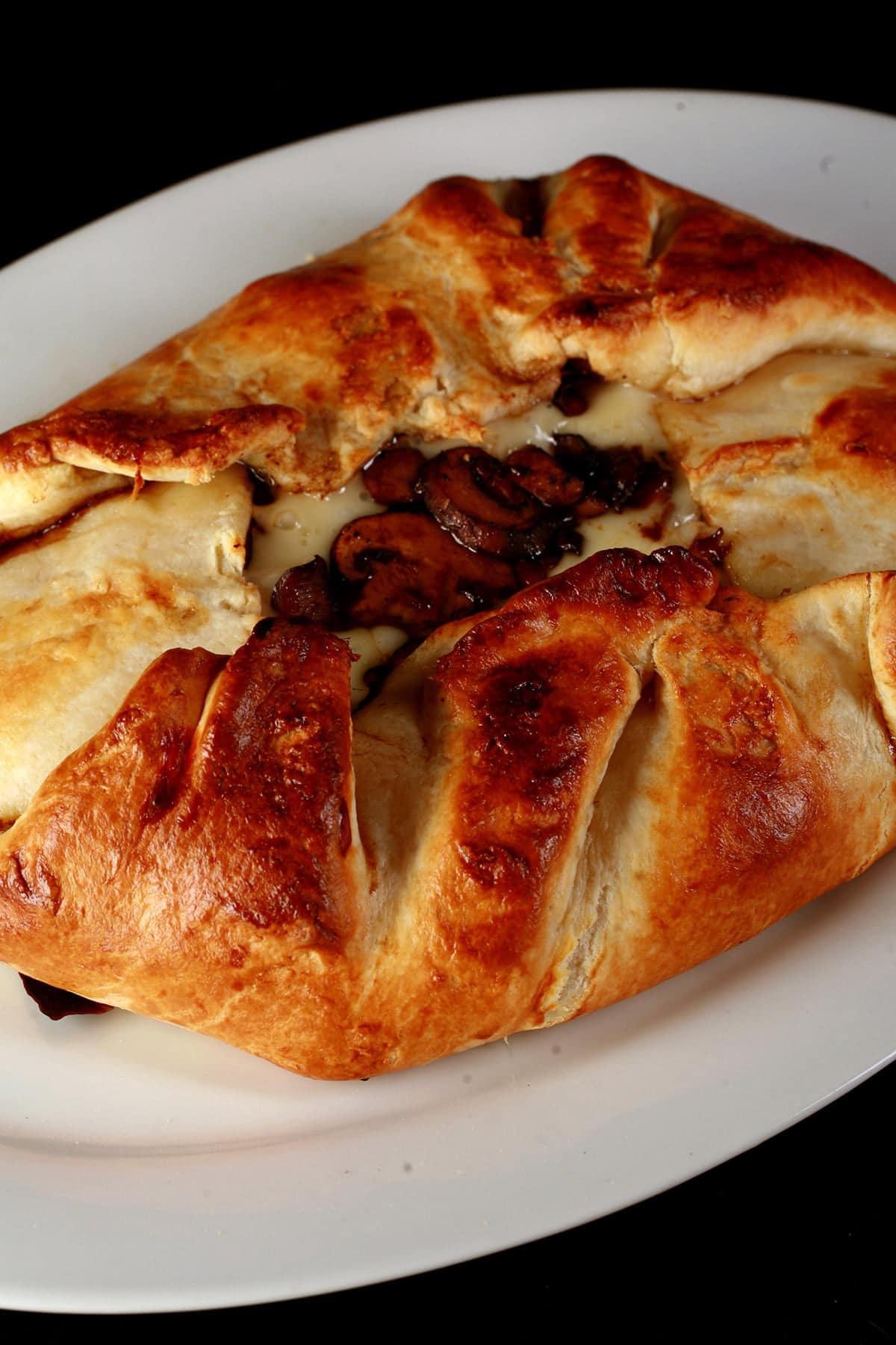An oval shaped baked brie. Melted cheese and mushrooms are visible in the center.